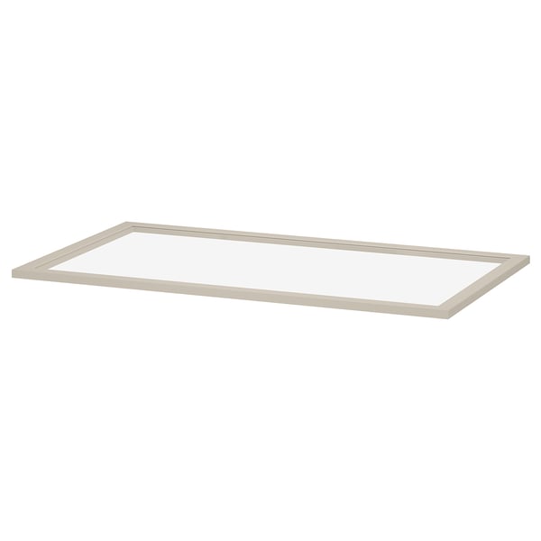 An ikea KOMPLEMENT glass shelf, clear and rectangular, framed in light beige. Its made of fibreboard and tempered glass, designed for pax wardrobes.