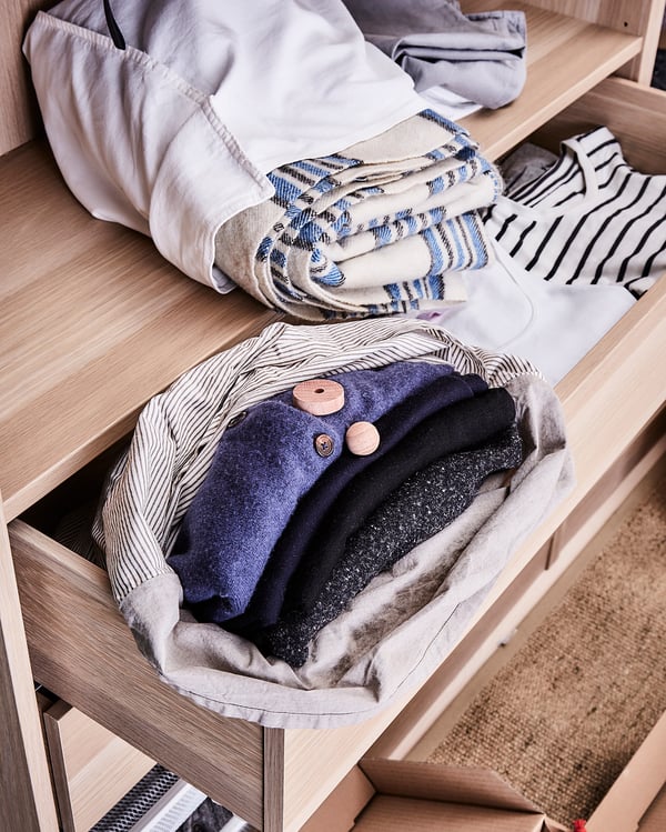 KOMPLEMENT light wood shelf, folded clothes including blue, white, striped, and black items. Neat, organised wardrobe storage.
