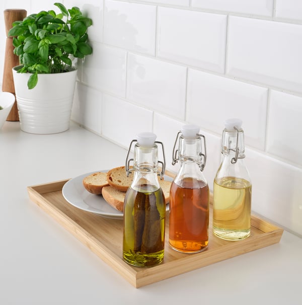 Three KORKEN bottles on tray, holding liquids, next to bread and plant.