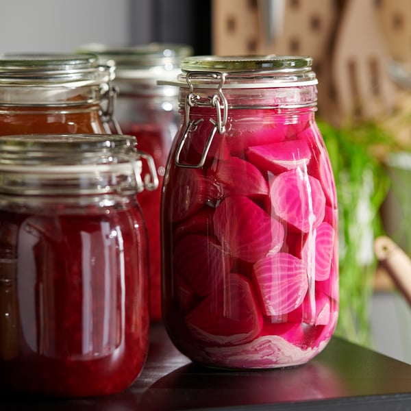 Three glass jars with metal clamps hold pickled vegetables, preserving their freshness. The transparent design allows contents to be easily seen.