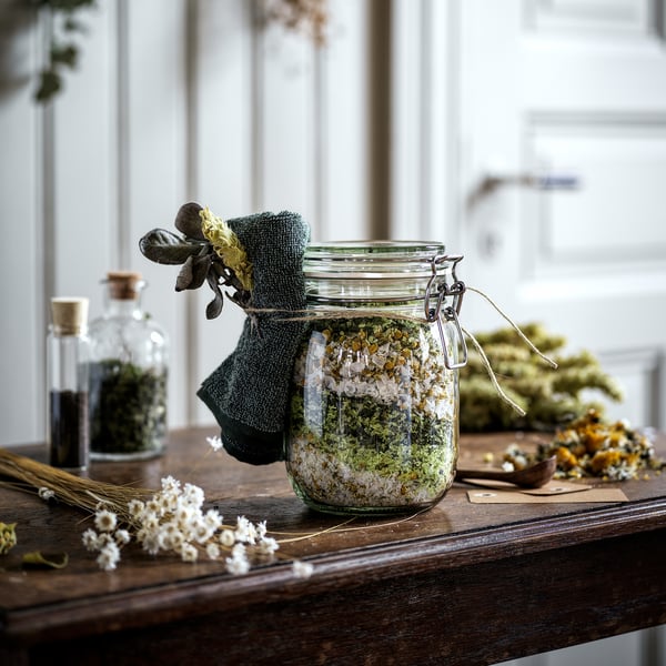 Jar with herbs and flowers on wooden table, sealed with an airtight lid.
