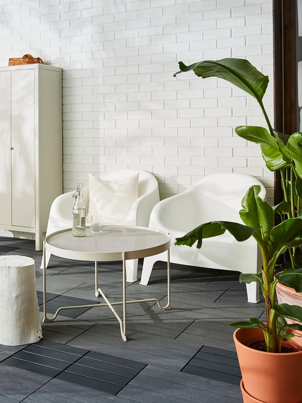 Modern minimalist patio featuring a krokhomen beige coffee table with a metal mesh top. White chairs, potted plant, and tiled floor.