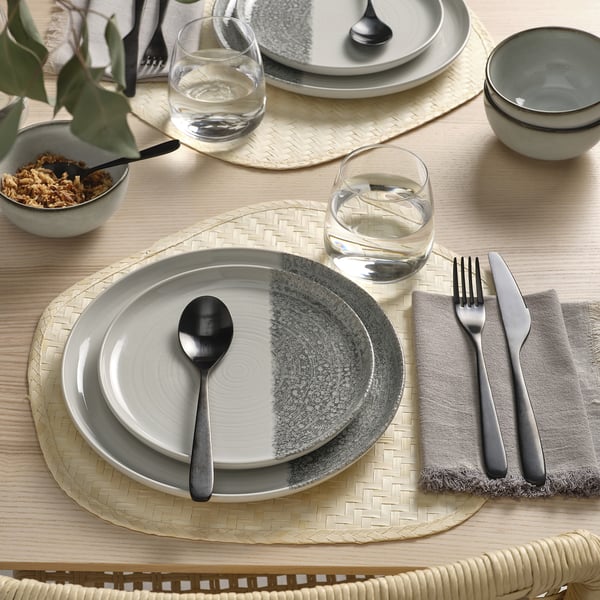 Grey KRUSTISTEL plates with cutlery, napkin, wine glass, and bowl on woven placemat.