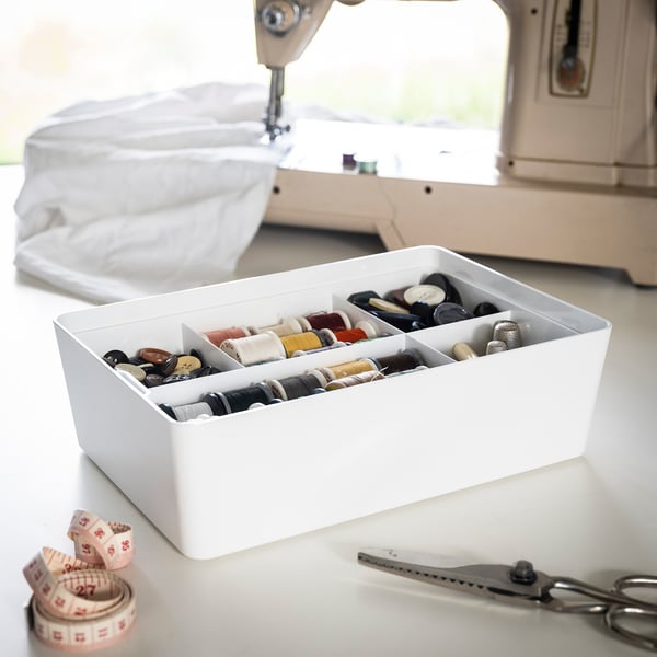 White KUGGIS box organises buttons, threads, and accessories, with scissors and tape.