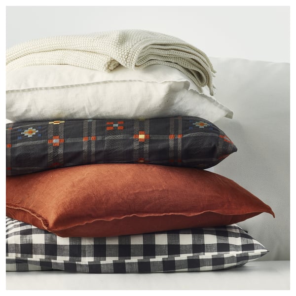 Stacked pillows: KUSTGRAN cushions in grey, red, black-white check, soft cotton, rectangular shape, varied patterns.