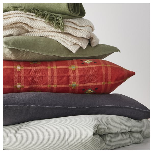Stack of colourful pillows: red, green, grey, and white; red has chequered monk’s belt pattern.