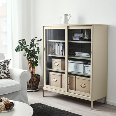 Modern beige KVARNVIK storage in living room with glass doors, showing books and decor.
