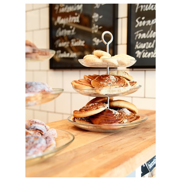 Modern glass serving stand with stainless-steel handle displays layered pastries in small plates, ideal for snacks.