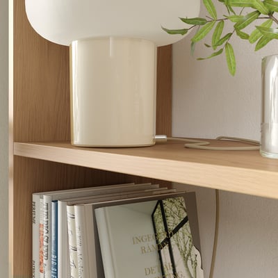 White LÅDMAKARE shelf made of particleboard, fiberboard, and plastic edging. It holds books and a small lamp.
