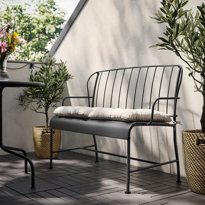 Modern outdoor black metal bench with white cushions against a light wall.