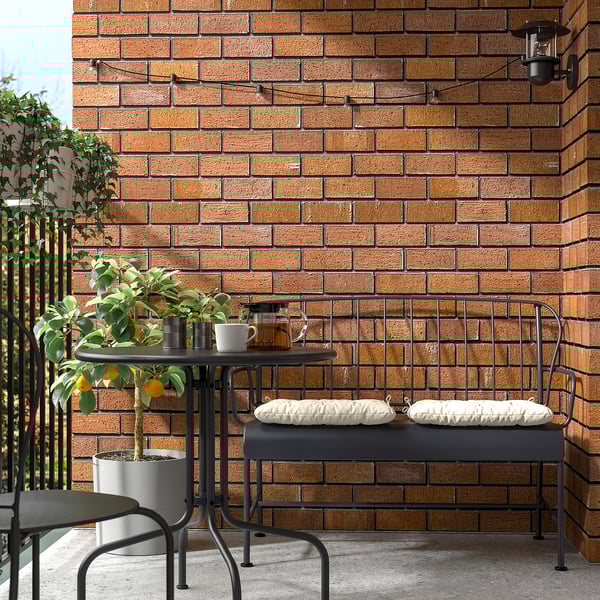 Small outdoor table set. Black metal design. Against brick wall. With two cushioned benches. Next to potted lemon tree.