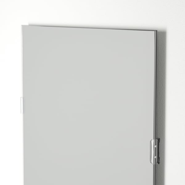 A sleek rectangular mirror with a thin frame hangs on a wall. The glass surface is clear, reflecting light for a bright effect.