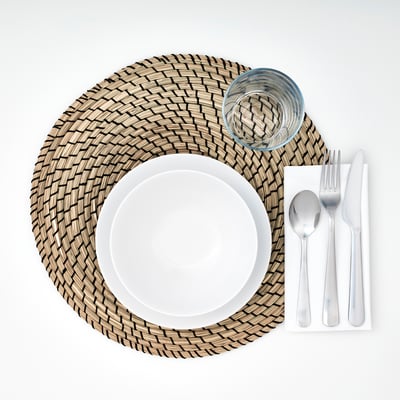 Round woven place mat with white plate, glass, and cutlery neatly arranged.