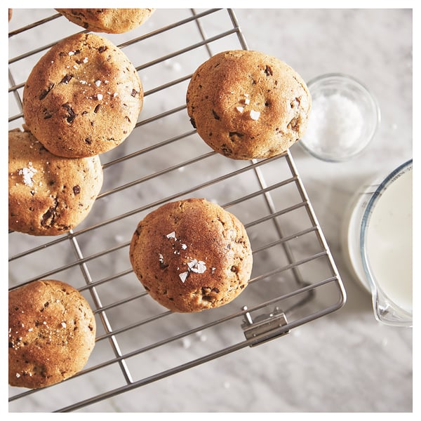 Five cookies on a stainless-steel wire rack, two glasses of milk beside, grey countertop.