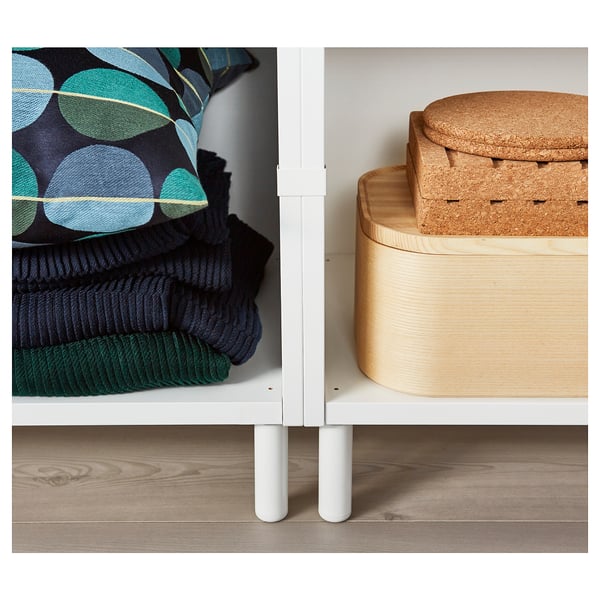 White storage unit with beech legs, folded blankets, and round wooden boxes.