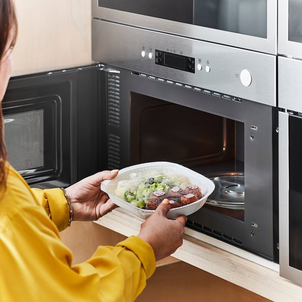 Person in yellow shirt placing microwaved LÄTTLAGAT meal into oven for heating.