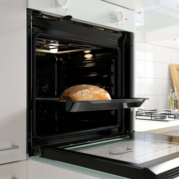 Black oven with bread baking inside, modern kitchen setting.