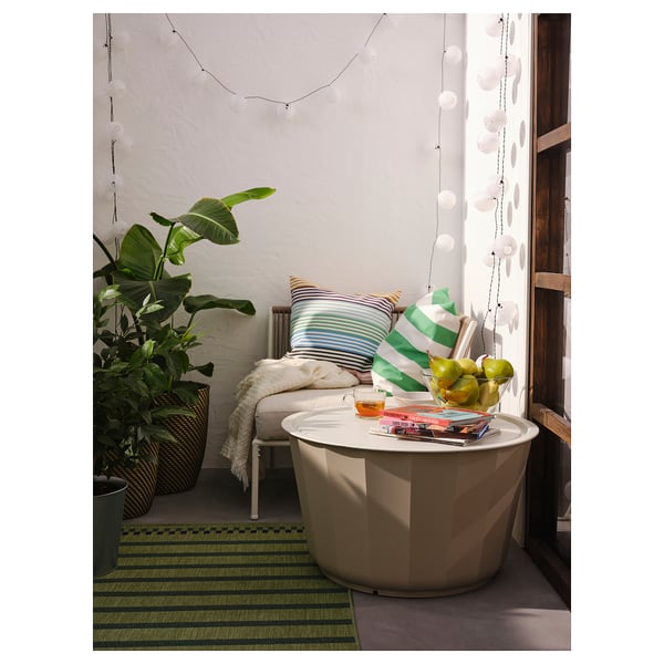 Modern outdoor corner with white LÅGASKÄR table, striped cushions, green rug, large plant, and hanging lights.