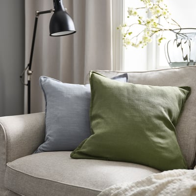 Cozy living room with grey-green cushion on beige sofa, blue pillow, lamp, and white flowers.