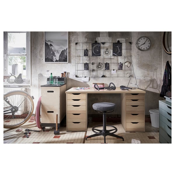Industrial-themed office space featuring LAGKAPTEN light wood desk with drawers, stool, and decorative wall art.
