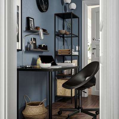 Modern home office setup: black desk, stylish chair, bookshelf with accessories, and blue wall.