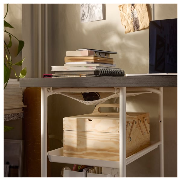 A LAGKAPTEN desk with a grey top and white legs, holding books, a laptop, and storage boxes.