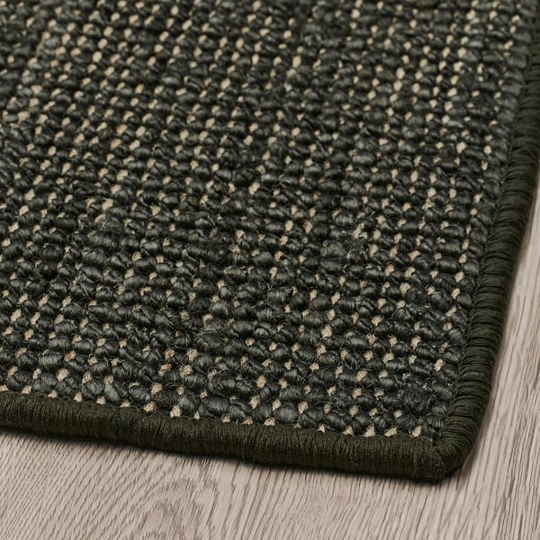 Jute door mat with beige flecks, black border, on wood floor.