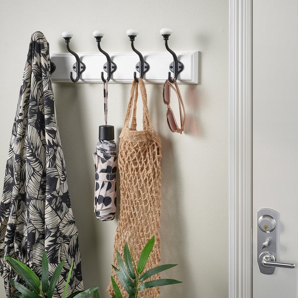 A white coat rack with five double hooks holds a jacket, umbrella, and bag; ideal for hallways.