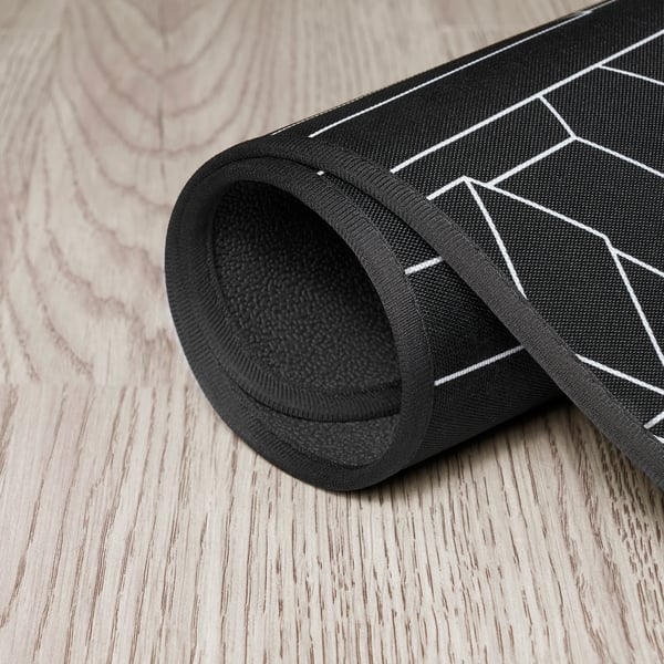Black roll-up gaming chair mat with geometric pattern, showcasing its textured underside for stability.