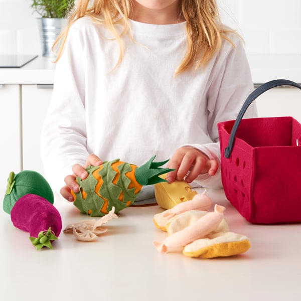 Child playing with LÅTSAS toy food, slicing pineapple at table.