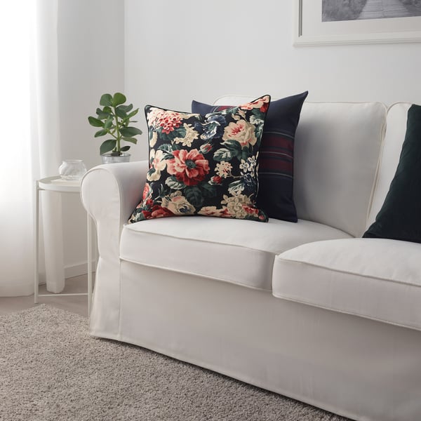 Bright floral pillow on white couch, smaller than plant, dark background, colourful flowers.