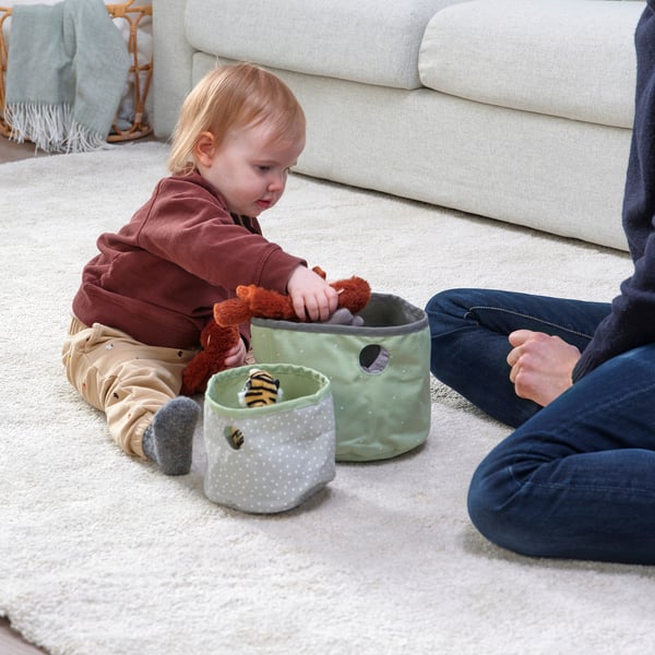 Child playing with reversible storage bags featuring bee, part of LENs sustainable collection, on a rug in living room.