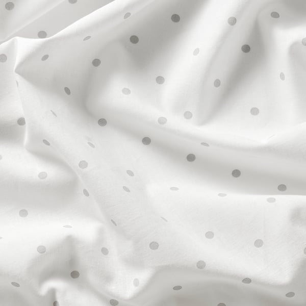 Soft, white cotton fabric with small grey dots, gently draped, showcasing quality texture and pattern.