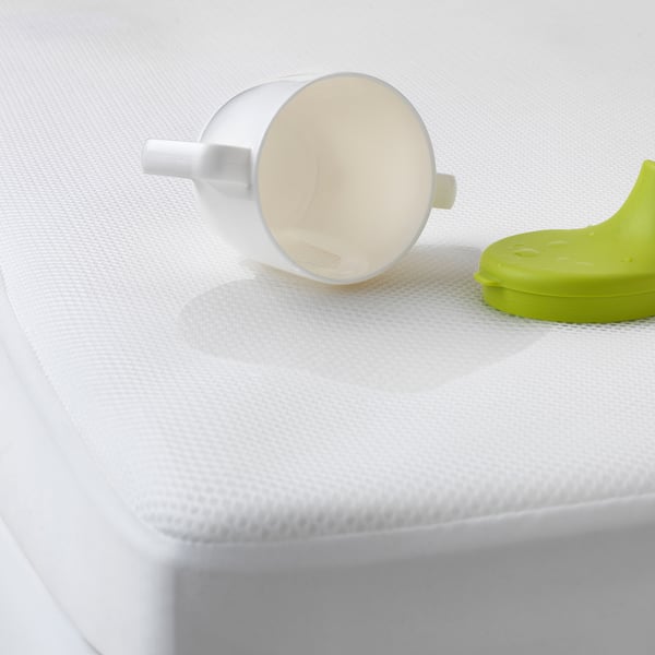 White mug tipped over on white mattress protector with green sippy cup nearby.
