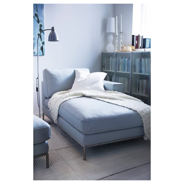 Modern living room with a blue LERSTA floor lamp and chair, white blanket, decorative shelf with vases and books, grey rug, and light grey walls.