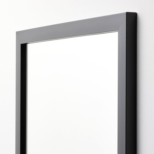 Modern wall mirror with sleek black frame, reflecting cleanly, securely mounted to light-colored wall.