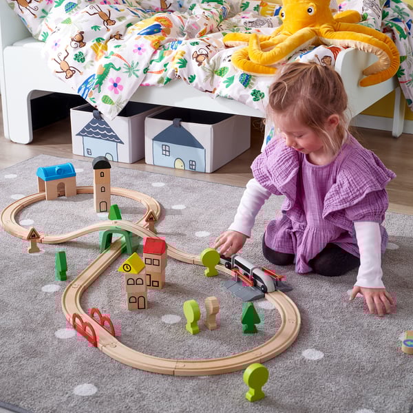 Child plays with colourful wooden train set, track has tunnels, bridges, buildings.