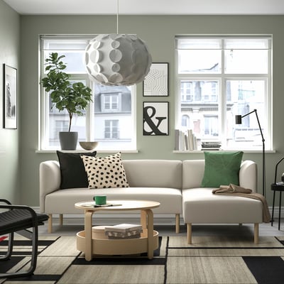 Modern living room with LILLEHEM beige sofa. Large windows, plant, unique light. Minimalist decor with black & white accents.