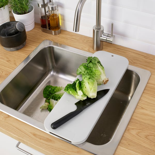 Cutting board over sink, chopping lettuce with knife.