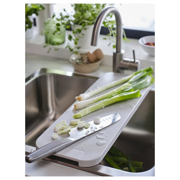 White LILLHAVET chopping board with green onions and knife near stainless sink.