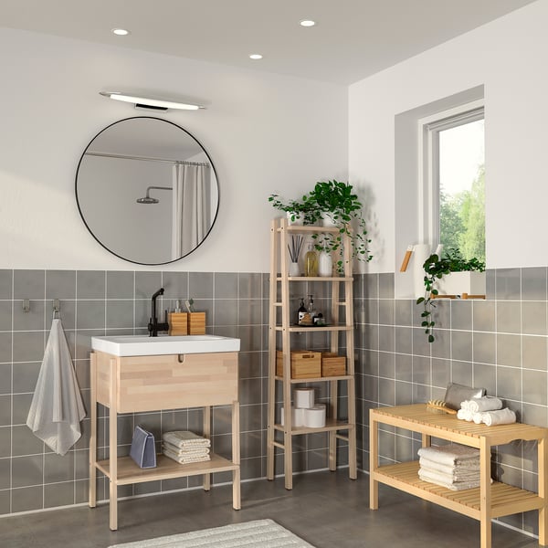 Modern bathroom with LINDBYN black mirror. Round, large mirror above light wood vanity. Plants and towels on wooden shelves.