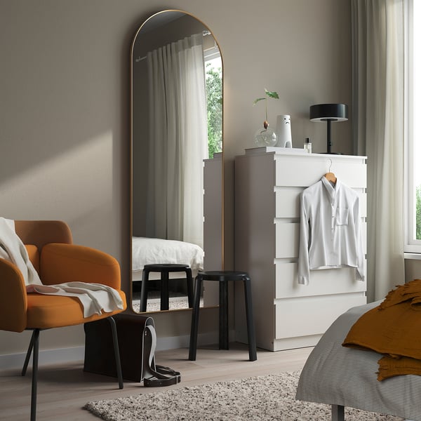 LINDBYN gold-framed mirror beside white dresser, complements modern decor.