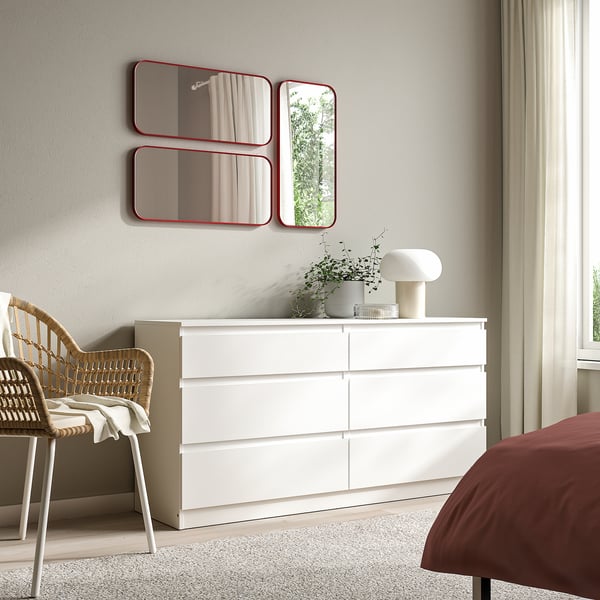 Modern bedroom: red mirrors, white dresser, wicker chair, red bed, lamp.