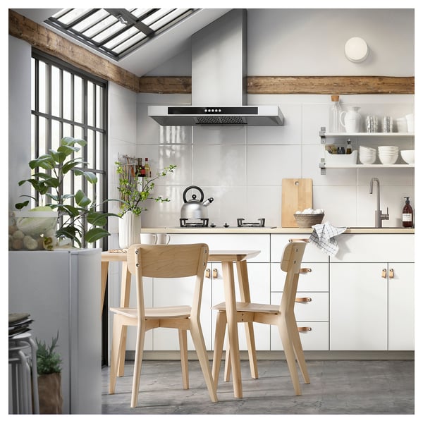 Minimalist kitchen with wooden dining set, white counter, plants, and skylight.