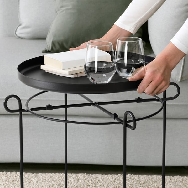 Person adjusting tray on LIVELYCKE side table with two glasses and a book, ideal for serving and storage.