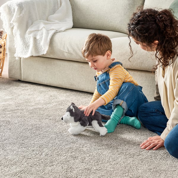 Child plays with husky toy on rug while adult watches.