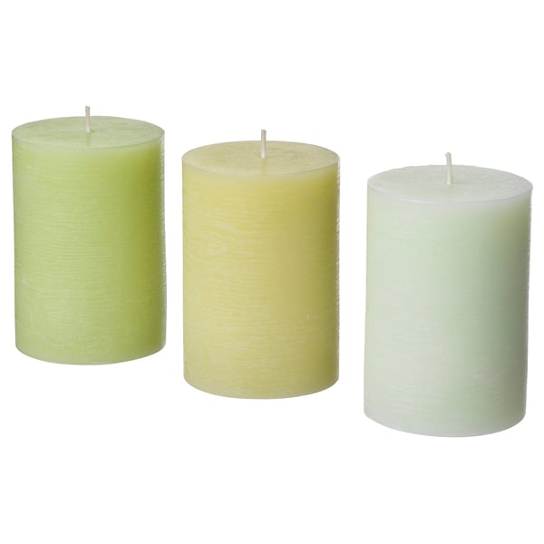 Three cylindrical candles in shades of green, cream, and white, each with a wick at the top, arranged in a row.