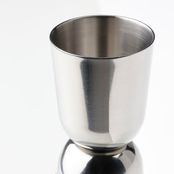 Shiny stainless steel cocktail shaker, polished surface reflecting light, stands alone on a reflective surface.