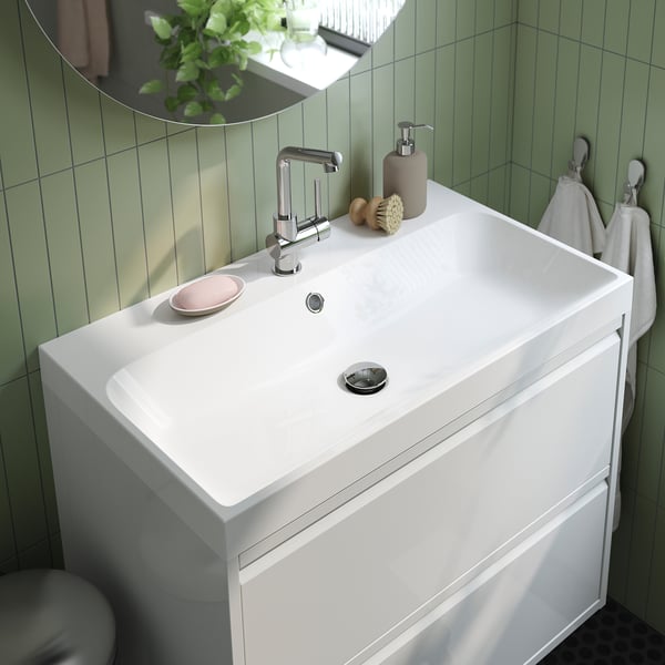 Modern white bathroom sink with chrome mixer tap, soap dispenser, and towels. Green tiled wall.