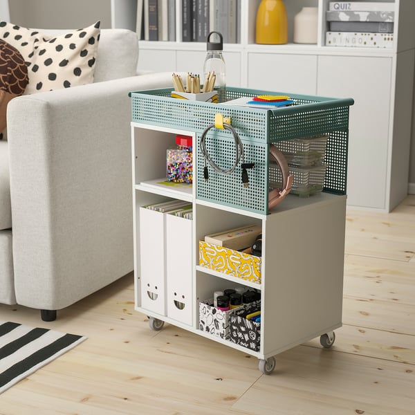 Minimalist home office with LYSMASK storage unit. Four green/white boxes on wheels, storing office supplies neatly near a chair and bookshelf.